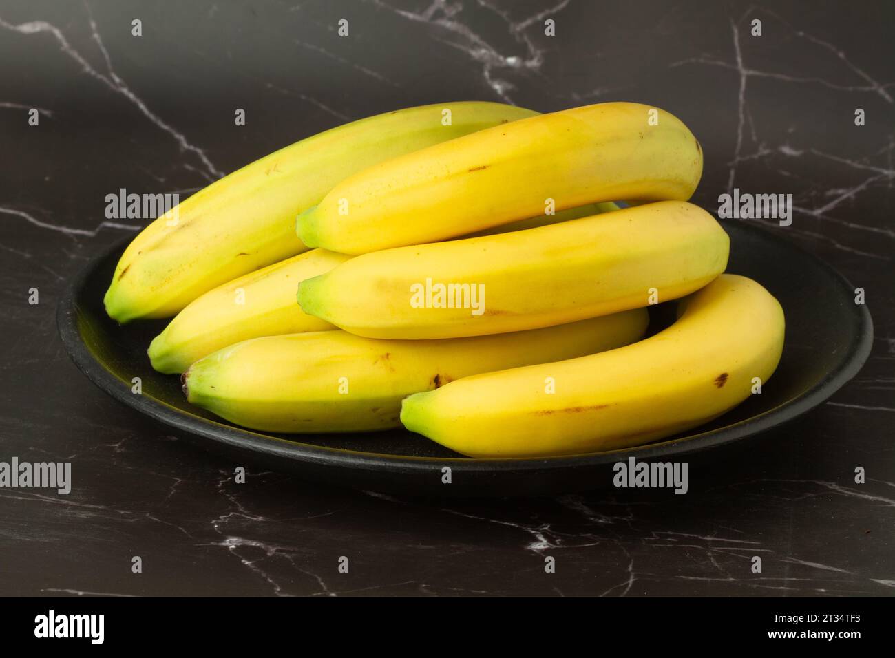 Bananen auf einem schwarzen Teller auf einer Küchenzeile aus schwarzem und weißem Marmor Stockfoto