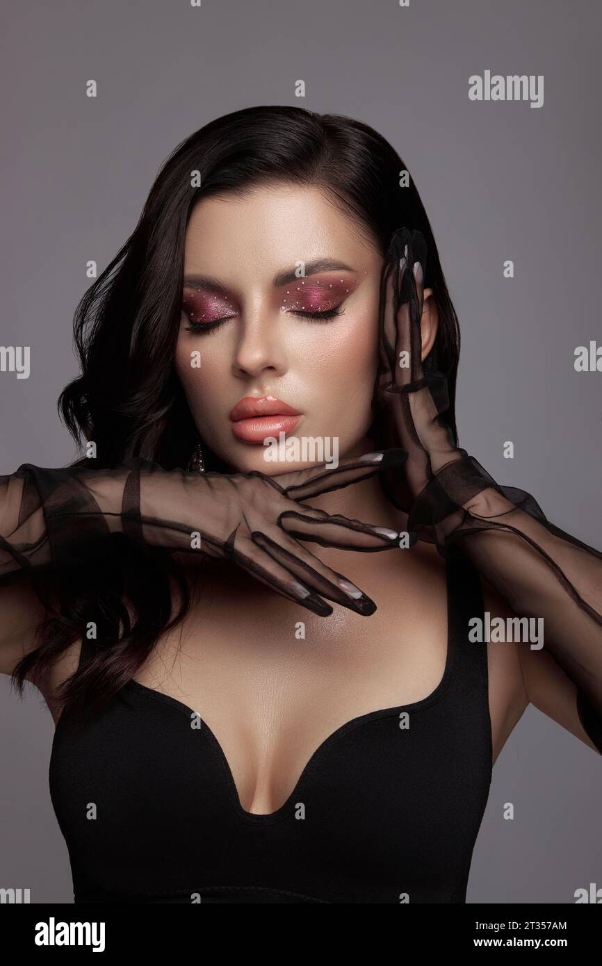 Beauty Porträt einer luxuriösen Frau mit rosa Make-up, sauberer Haut, schwarzen Handschuhen, Schleier an den Händen, Abendlook Stockfoto
