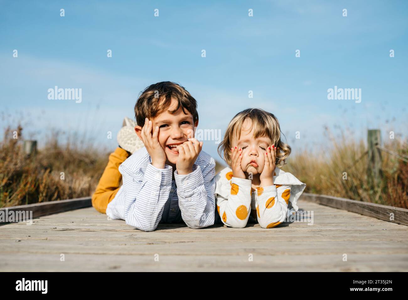 Portrait von Jungen und seine kleine Schwester liegen nebeneinander auf der Promenade ziehen lustige Gesichter Stockfoto