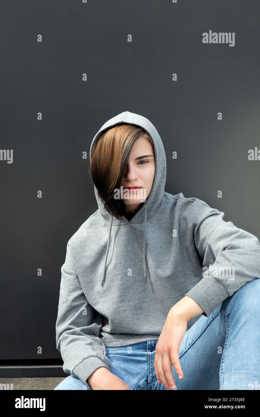 Teenager-Mädchen in Kapuzenhemd, das vor grauem Hintergrund sitzt Stockfoto