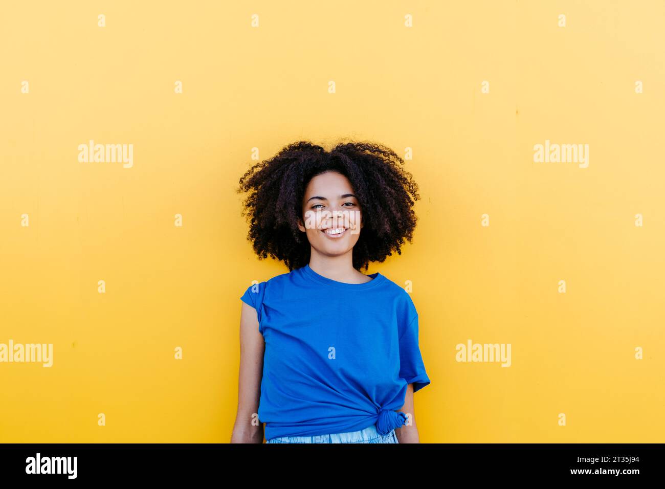 Hübsche Frau, die vor der gelben Wand steht und glücklich lächelt Stockfoto