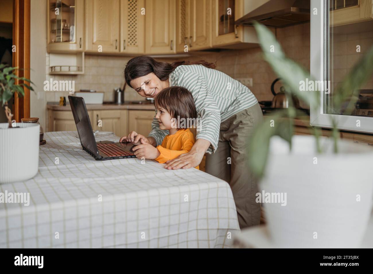 Mutter hilft dem Sohn, Online-Unterricht auf Laptop am Esstisch zu sehen Stockfoto