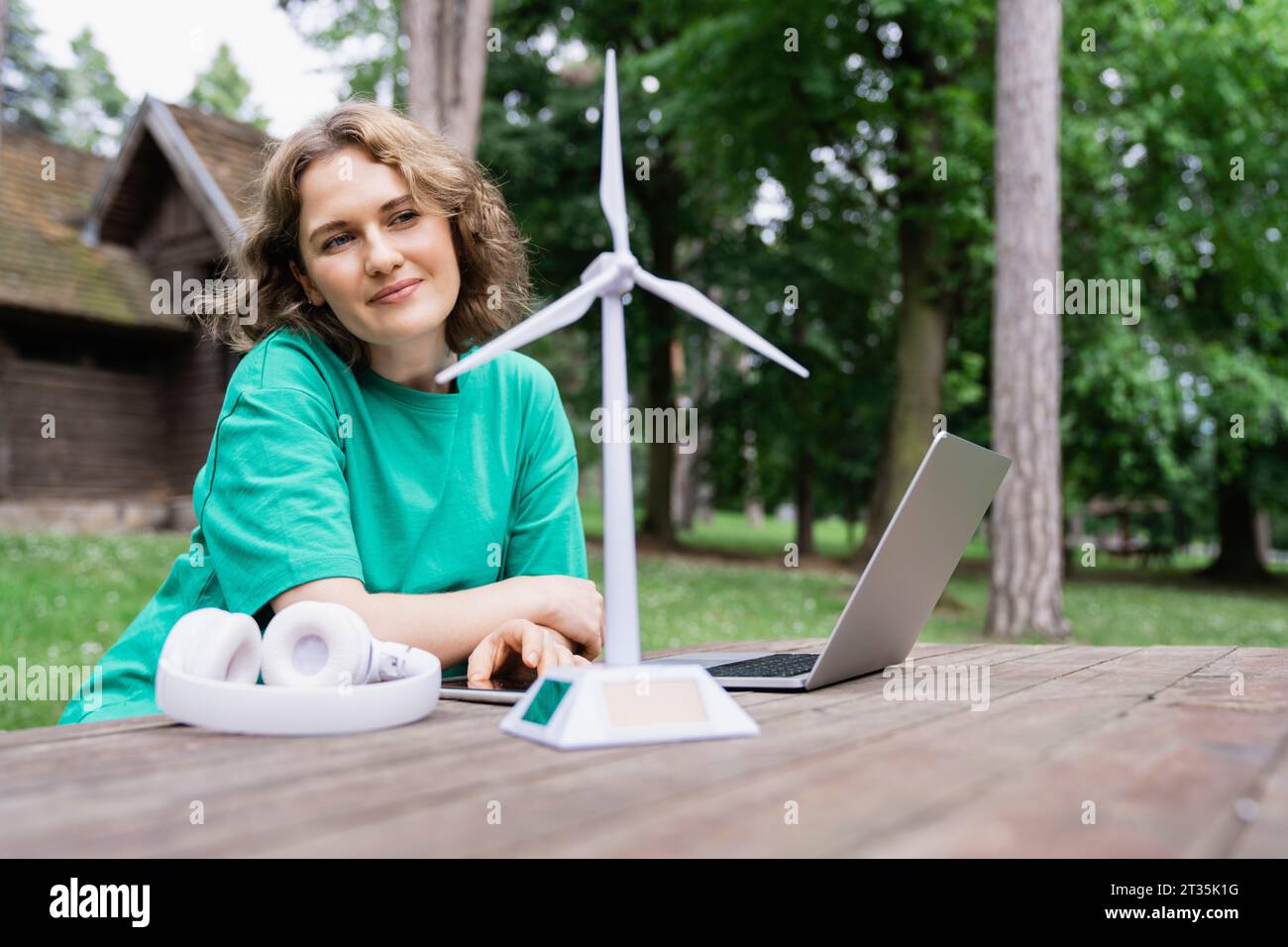 Geschäftsfrau, die sich ein Windkraftanlagenmodell mit drahtlosen Technologien auf dem Tisch im Wald ansieht Stockfoto