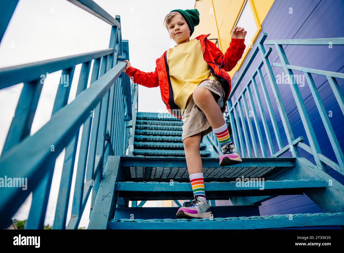 Junge in roter Jacke, der auf einem Bein auf einer Metalltreppe steht Stockfoto