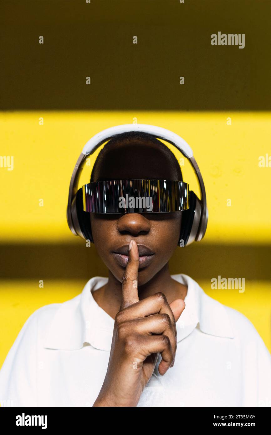 Geschäftsfrau mit dem Finger auf der Lippe, die kabellose Kopfhörer und eine intelligente Brille trägt Stockfoto