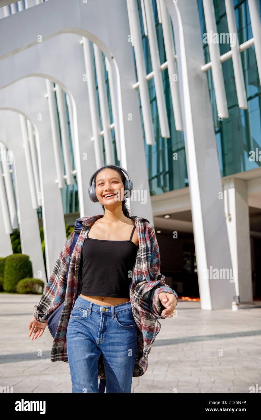 Glücklicher Student, der Musik hört und vor dem Universitätsgebäude spaziert Stockfoto