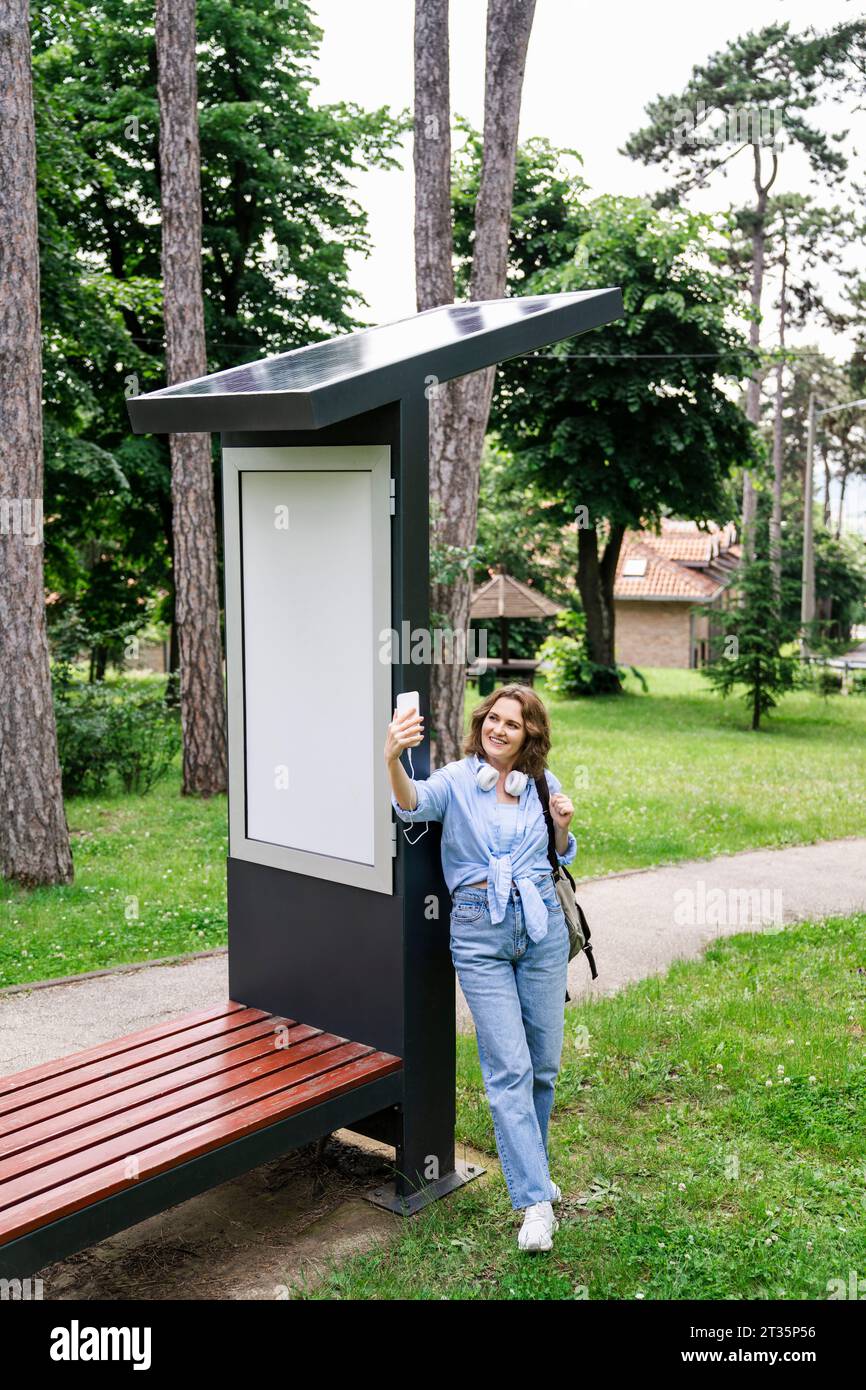 Frau, die Selfie durch Smartphone in der Nähe der Solarladestelle im Park macht Stockfoto