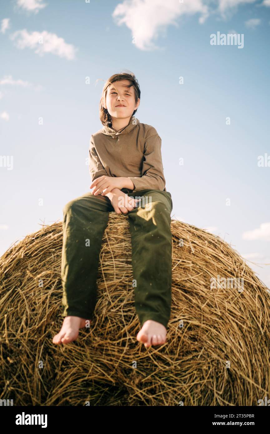 Junge sitzt auf Heuhaufen mit Himmel im Hintergrund Stockfoto