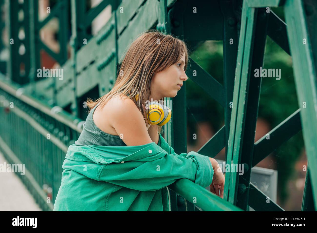 Durchdachtes Mädchen mit kabellosen Kopfhörern, die auf dem Geländer sitzen Stockfoto