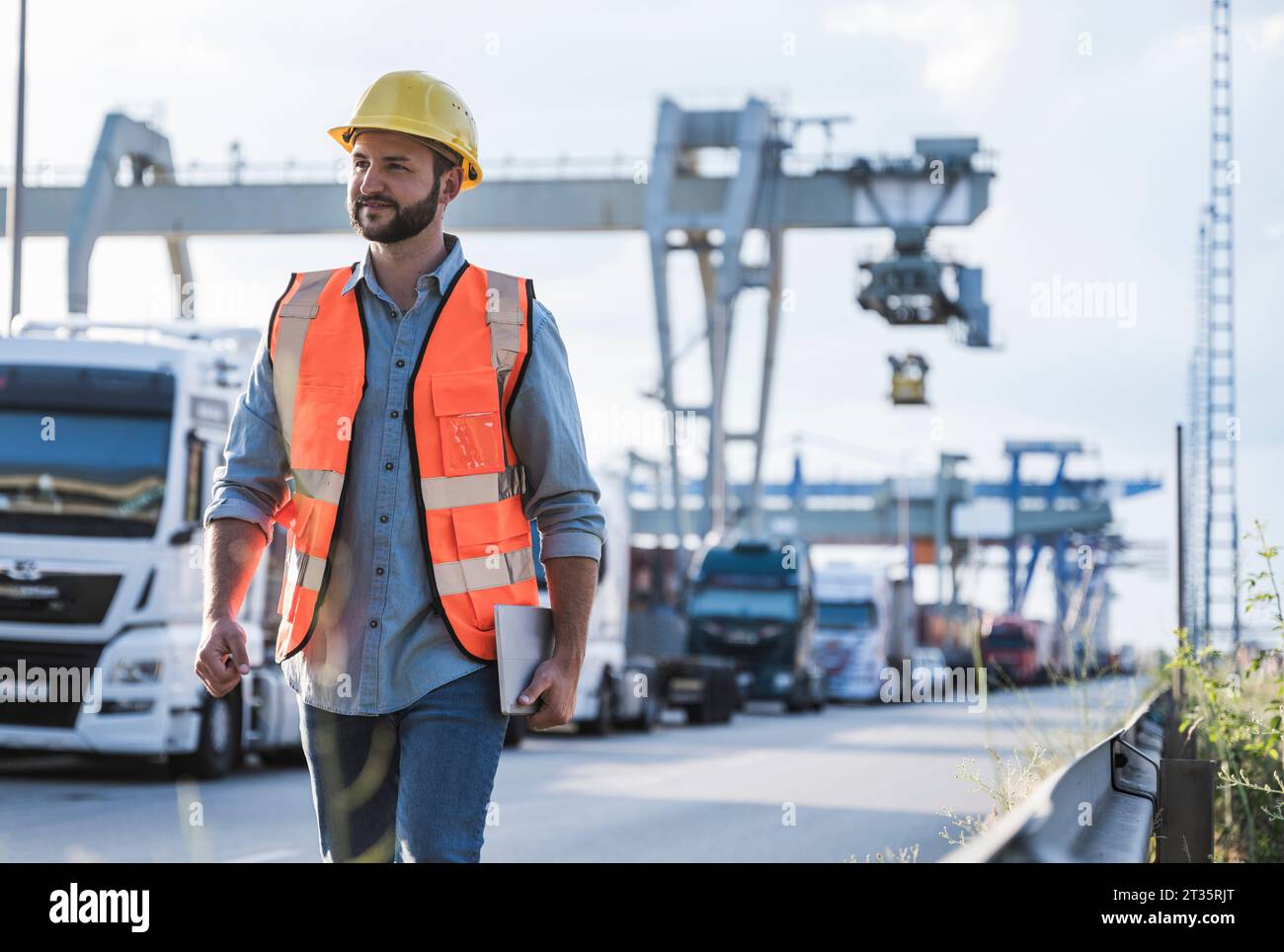 Lächelnder Logistikmitarbeiter, der mit einem Tablet-PC im Industrieviertel unterwegs ist Stockfoto