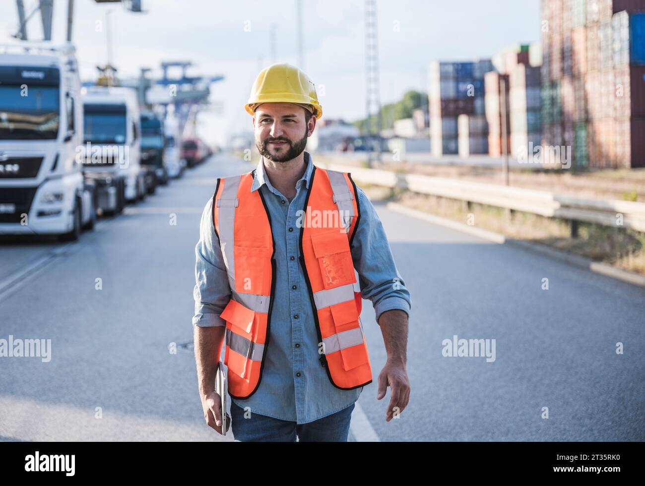 Lächelnder Logistikmitarbeiter mit Schutzhelm und unterwegs mit Tablet-PC Stockfoto