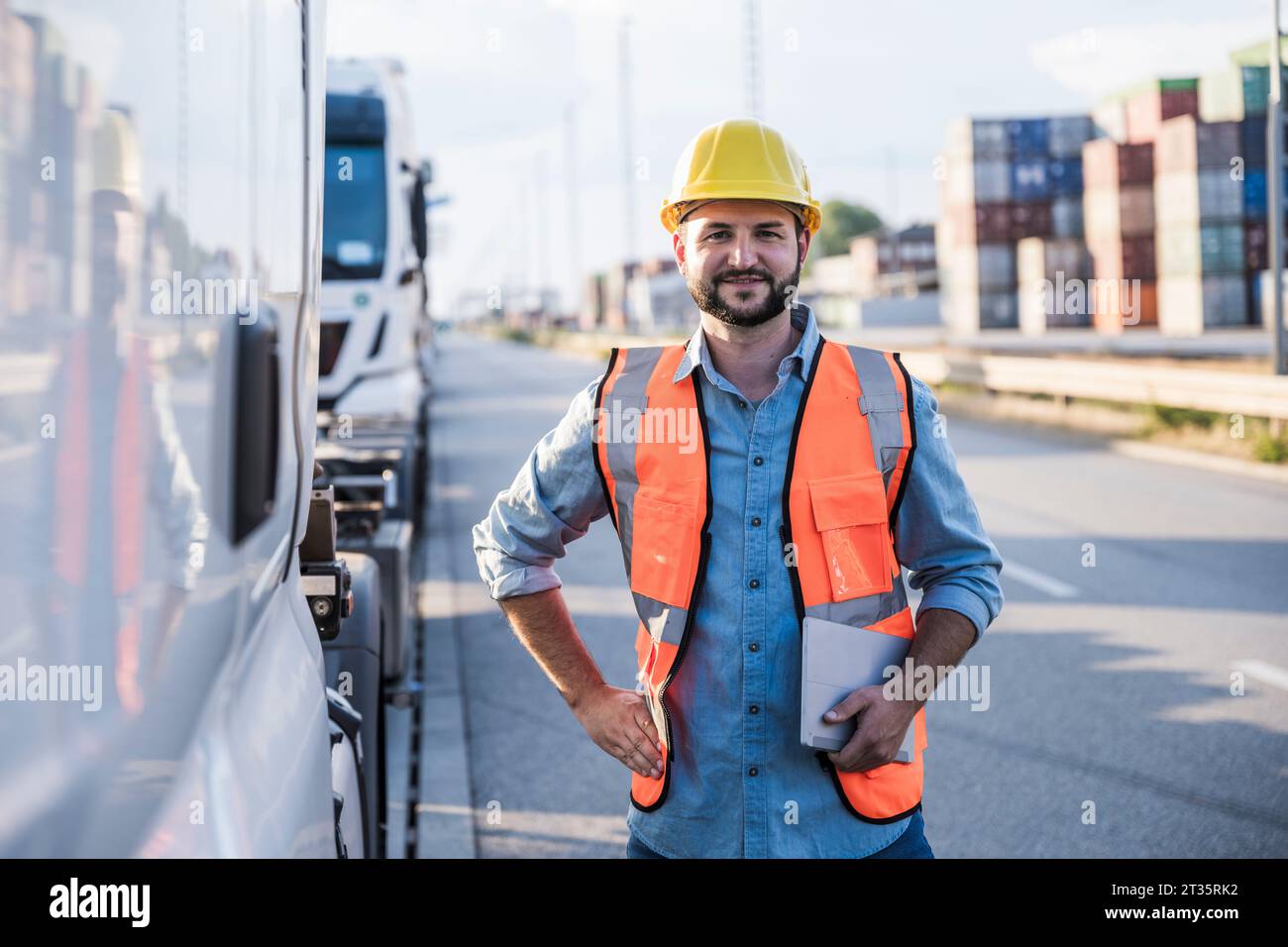 Lächelnder Logistikmitarbeiter, der mit Tablet-PC und Hand auf Hüfte steht Stockfoto