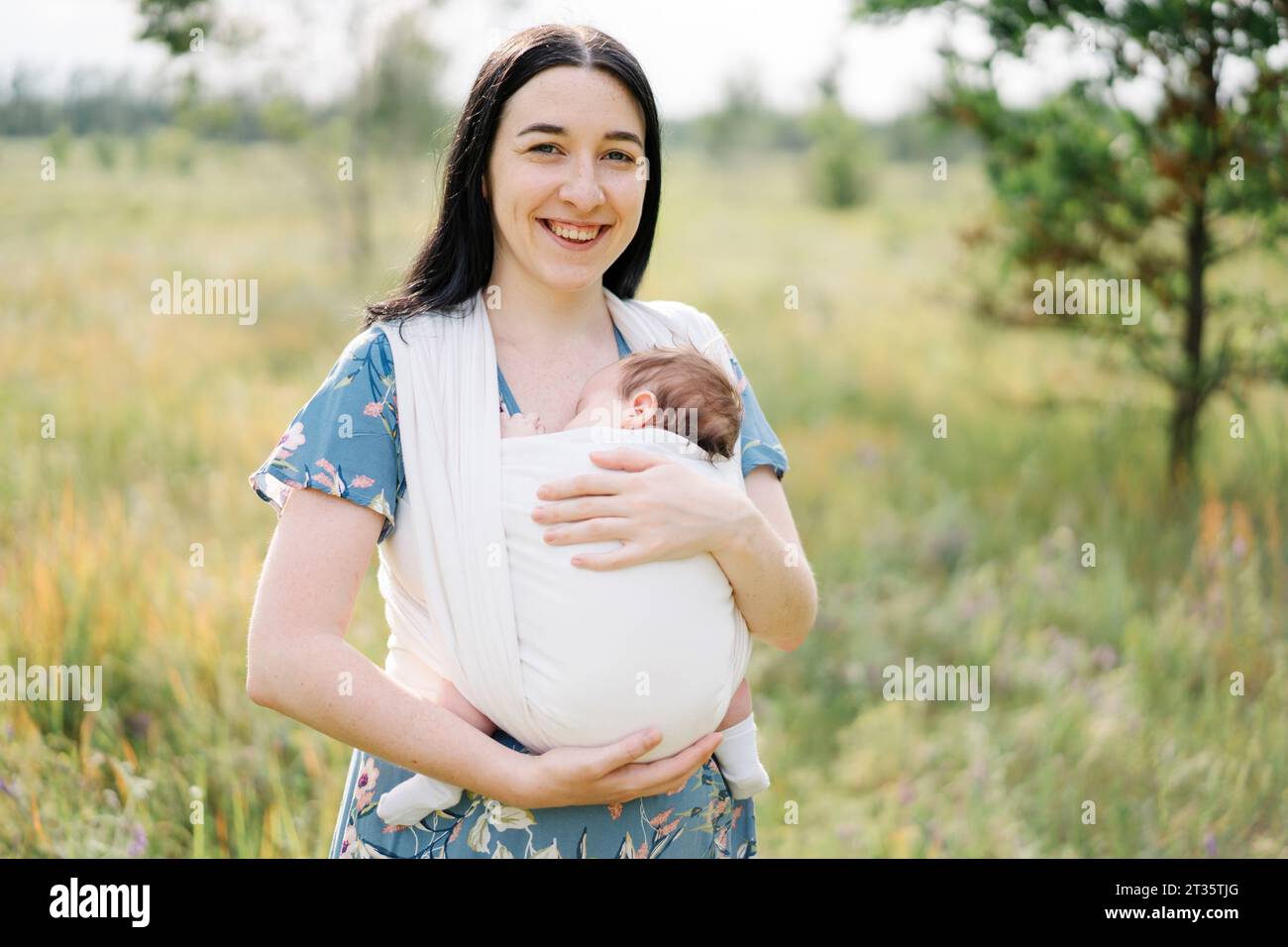Lächelnde Mutter, die Tochter in Babyschlinge trägt Stockfoto