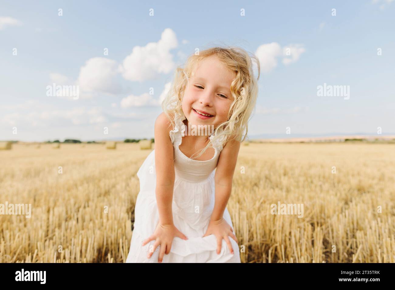 Glückliches blondes Mädchen, das auf einem Stoppelfeld steht und Hände auf den Knien hat Stockfoto