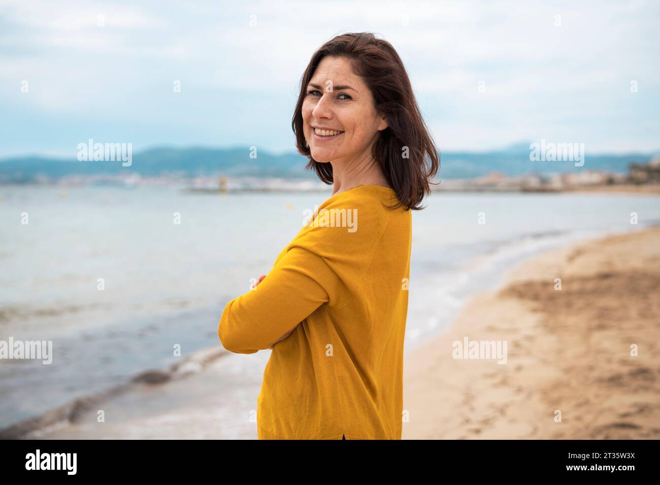 Glückliche Frau, die mit gekreuzten Armen am Strand steht Stockfoto