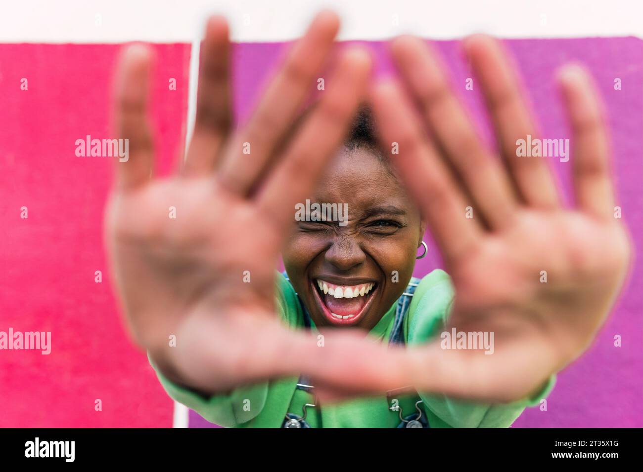 Fröhliche junge Frau mit Stop-Geste vor einer mehrfarbigen Wand Stockfoto