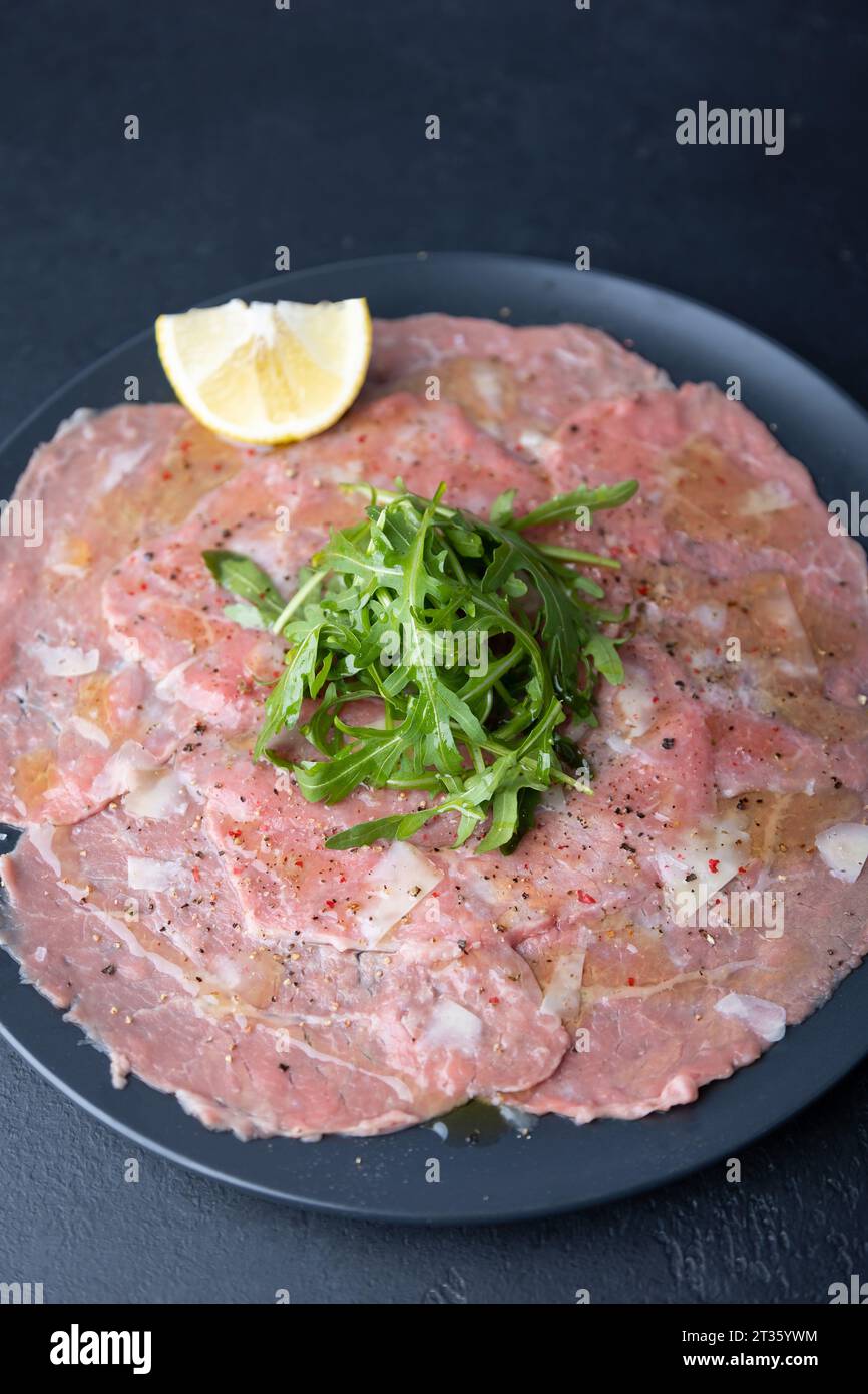 Marmorfleisch-Carpaccio mit Rucola, Parmesankäse, Olivenöl und Zitrone. Eine traditionelle klassische Vorspeise aus dünn geschnittenem rohem Fleisch. Nahaufnahme, Stockfoto