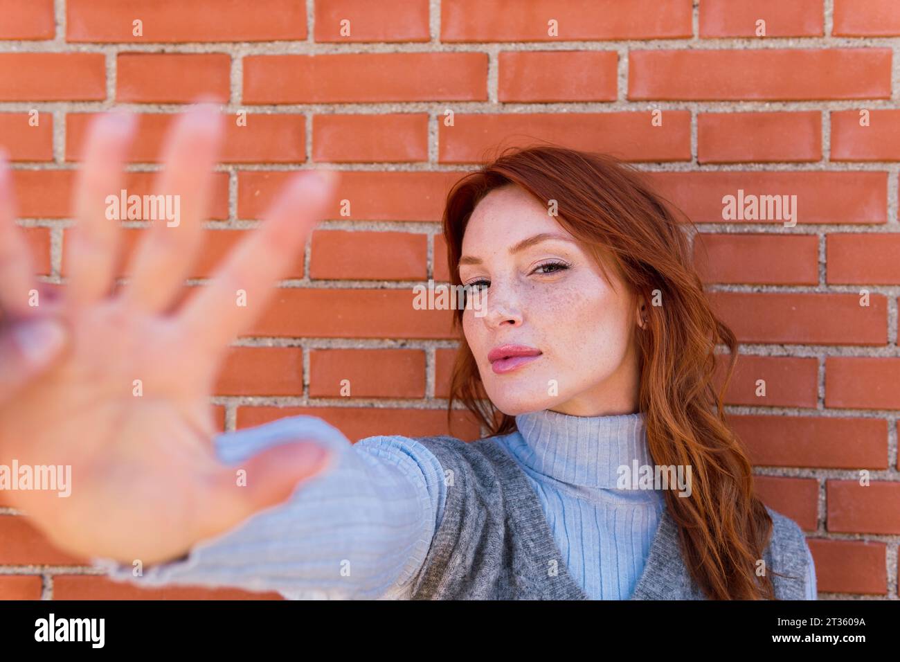 Frau zeigt Stoppgeste vor einer Ziegelmauer Stockfoto