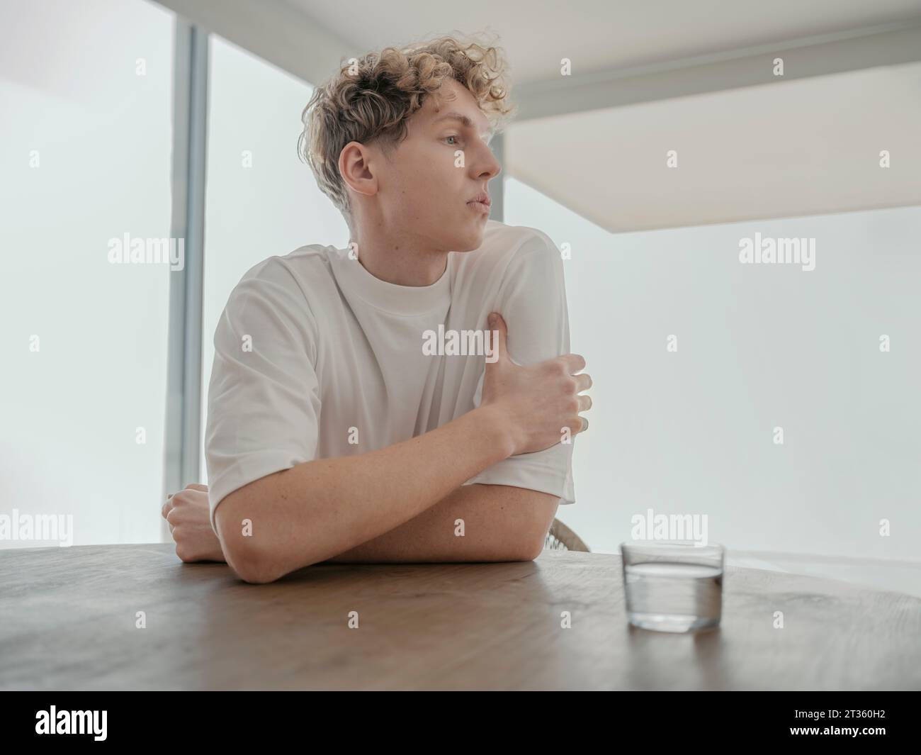 Ein nachdenklicher Mann sitzt zu Hause mit einem Glas Wasser am Tisch Stockfoto