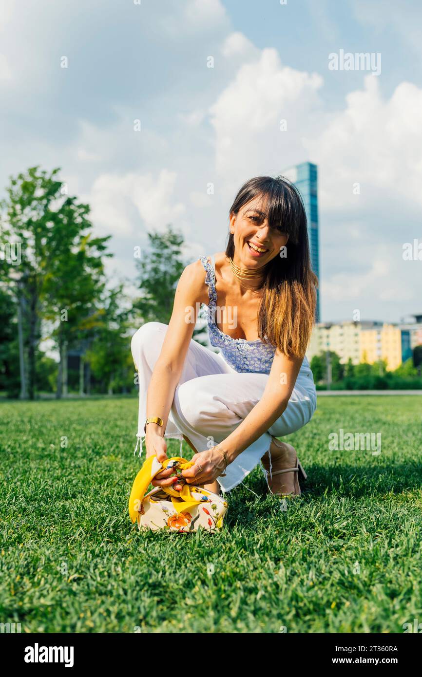 Glückliche Frau, die sich unter bewölktem Himmel auf Gras hockt Stockfoto