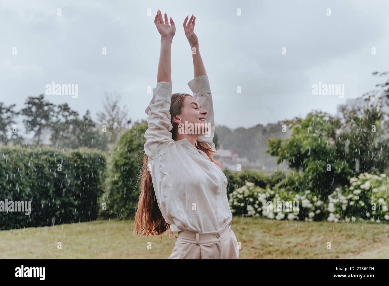Lächelnde Frau genießt im Garten den Regen Stockfoto