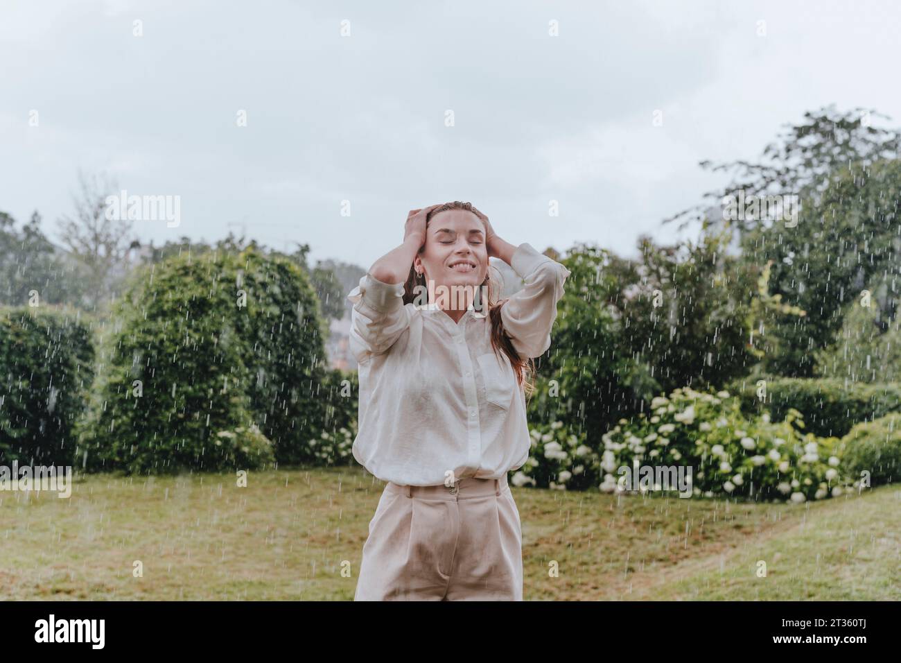 Glückliche Frau mit geschlossenen Augen, die im Regen im Garten genießt Stockfoto