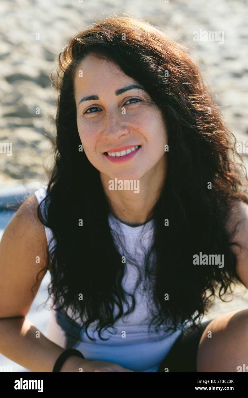 Glückliche Frau mit langen schwarzen Haaren am Strand an sonnigem Tag Stockfoto