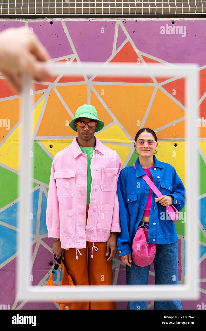 Eine zugeschnittene Hand hält einen Freund mit einem Paar, das vor einer bunten Wand steht Stockfoto