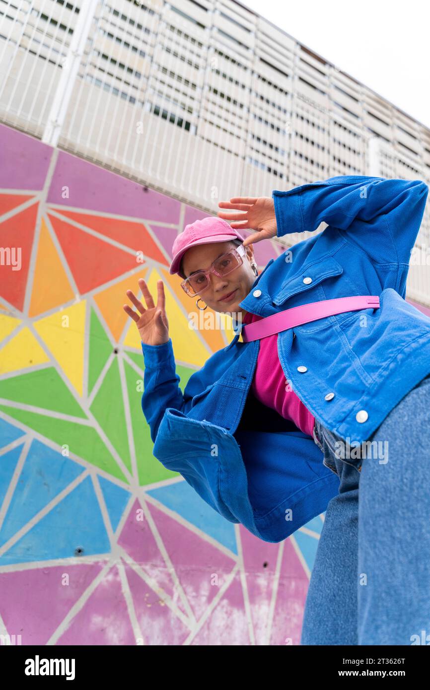 Hippe Frau mit blauer Jacke, die vor der bunten Wand gestickt ist Stockfoto