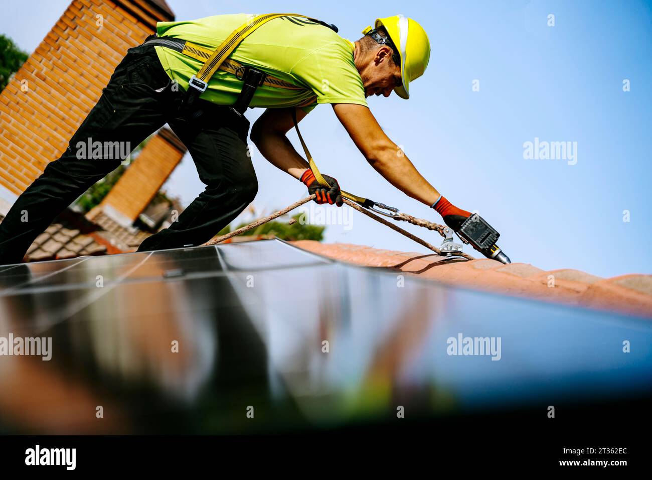 Ingenieur trägt Helm mit Bohrmaschine, um Solarpanel auf dem Dach zu installieren Stockfoto