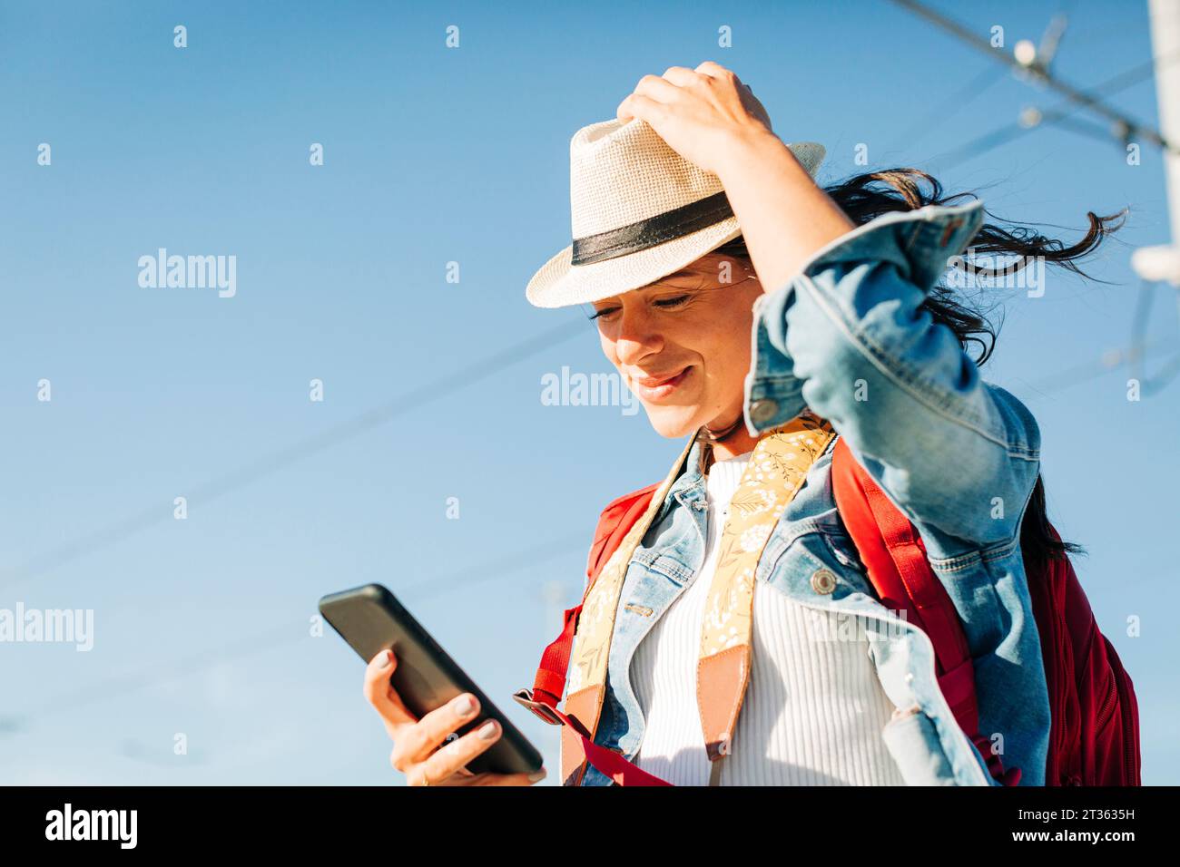 Lächelnde junge Frau, die unter dem Himmel ein Smartphone benutzt Stockfoto