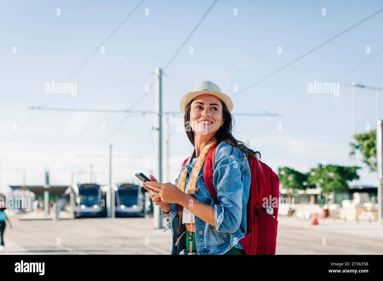 Glückliche junge Frau mit Handy, die am sonnigen Tag steht Stockfoto