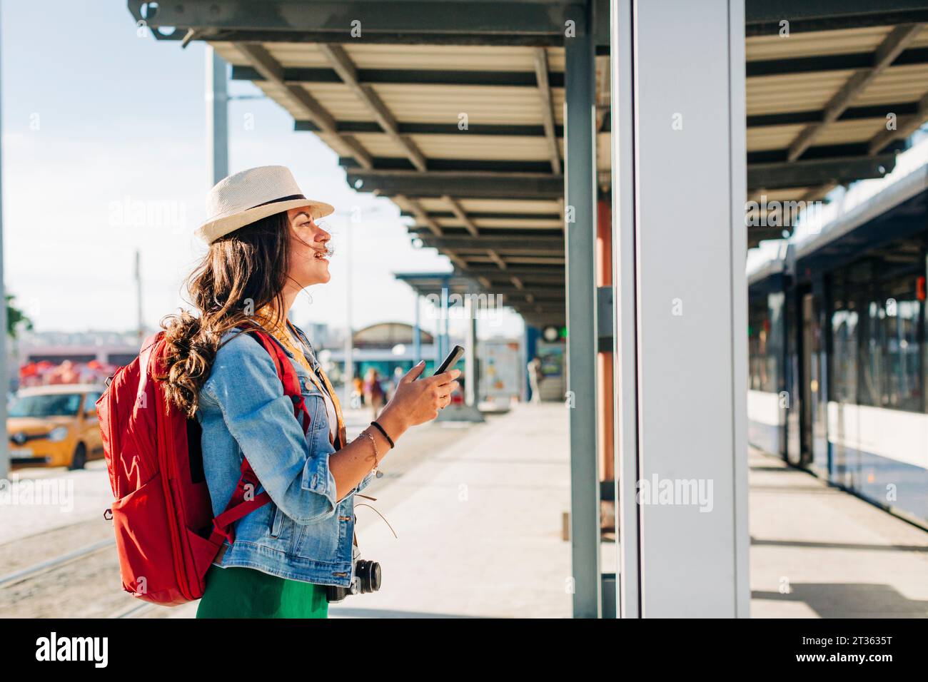 Eine junge Frau mit Hut, die an der Straßenbahnhaltestelle durch den Streckenplan geht Stockfoto