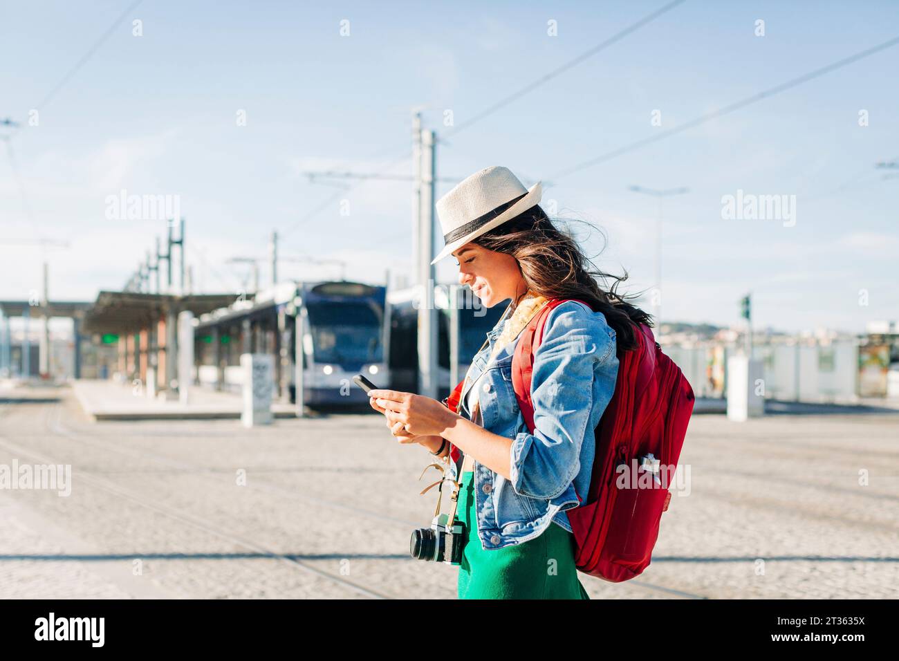 Lächelnde junge Frau, die am sonnigen Tag einen Hut mit Smartphone trägt Stockfoto