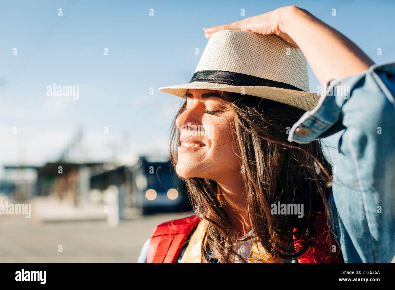Lächelnde junge Frau mit Hut und geschlossenen Augen an sonnigem Tag Stockfoto