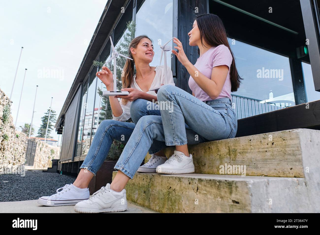 Zwei Ingenieurinnen reden draußen mit Windturbinenmodellen in der Hand Stockfoto