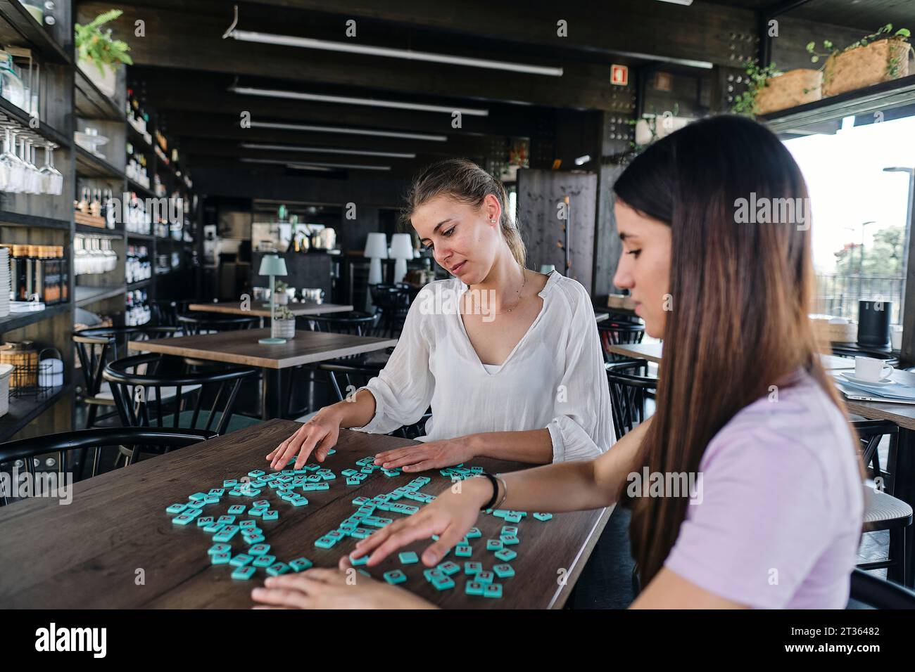 Zwei junge Frauen spielen Wortspiel am Café-Tisch Stockfoto