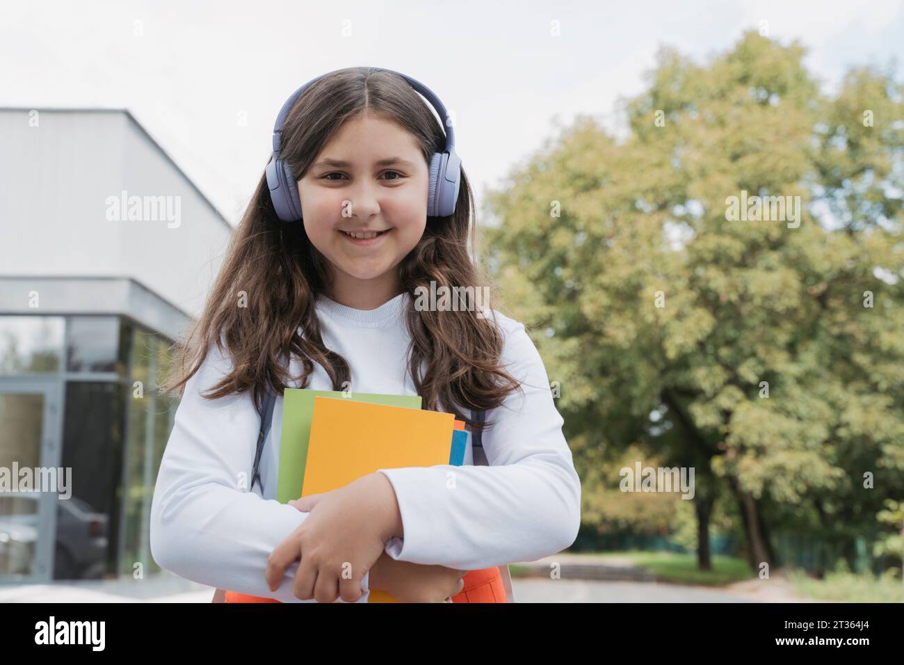 Lächelndes Schulmädchen mit kabellosen Kopfhörern und Büchern Stockfoto