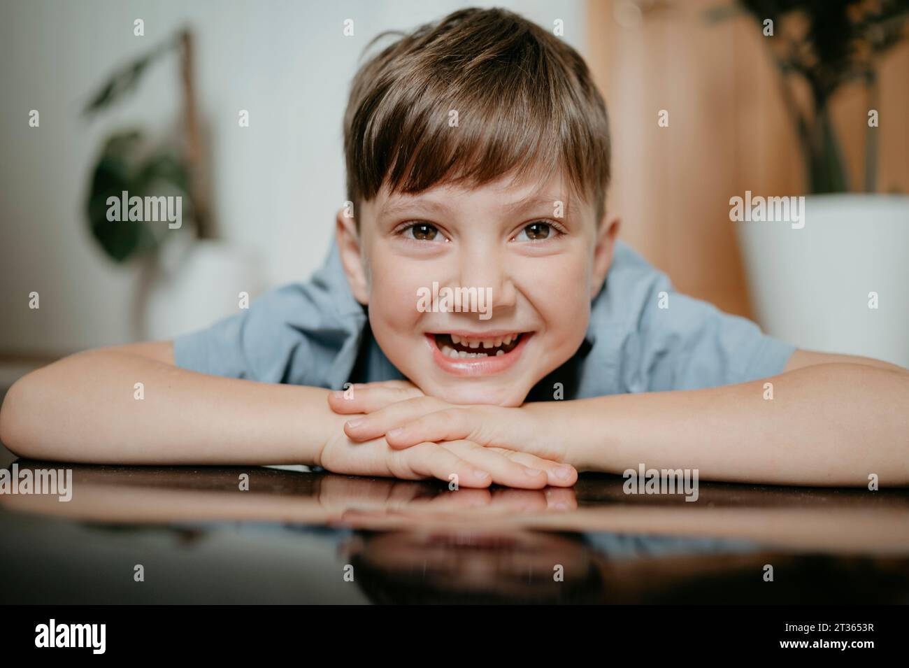 Lächelnder Junge mit Kopf auf den Armen zu Hause Stockfoto