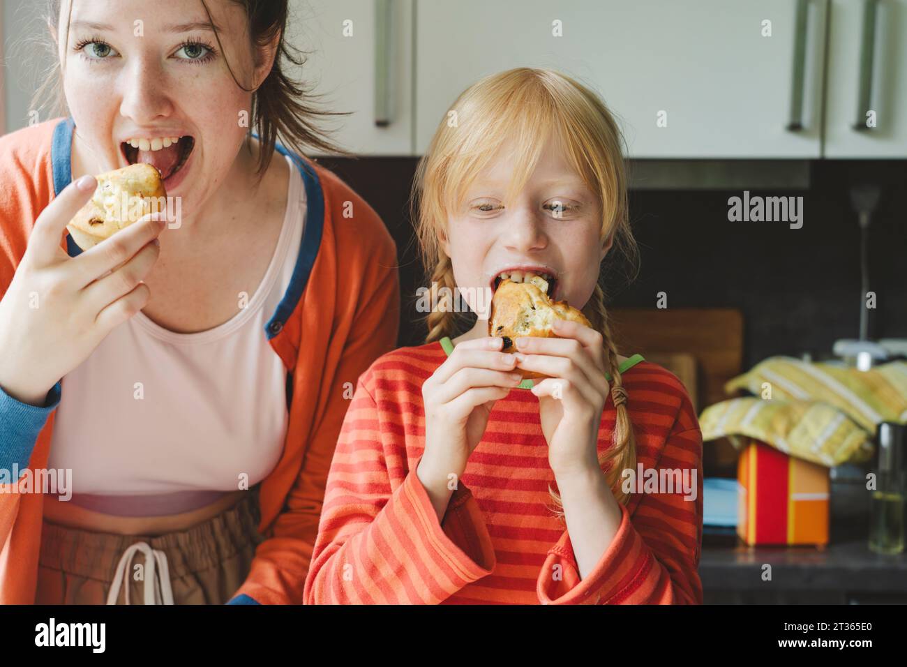 Teenager und ihre jüngere Schwester essen gebackene Muffins in der Küche Stockfoto