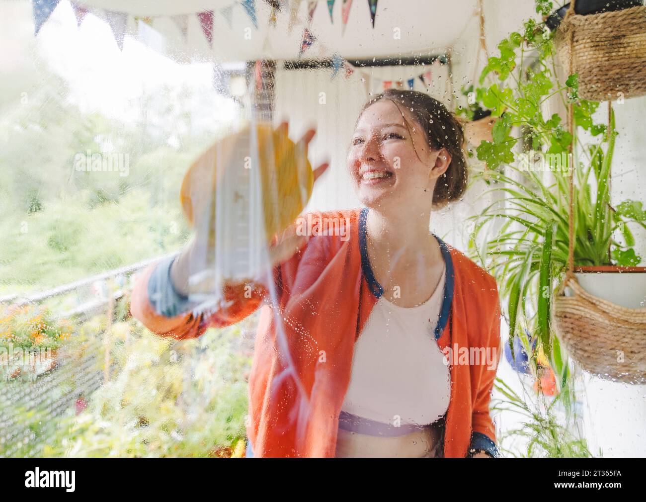 Glückliches Teenager-Mädchen, das die Balkontür sauber macht Stockfoto