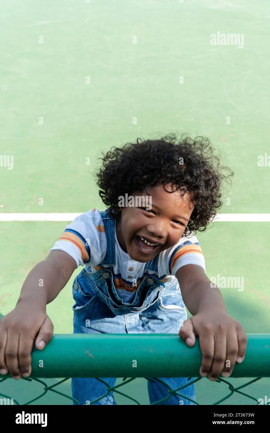 Lächelnder Junge, der einen Zaun auf dem Sportplatz hält Stockfoto