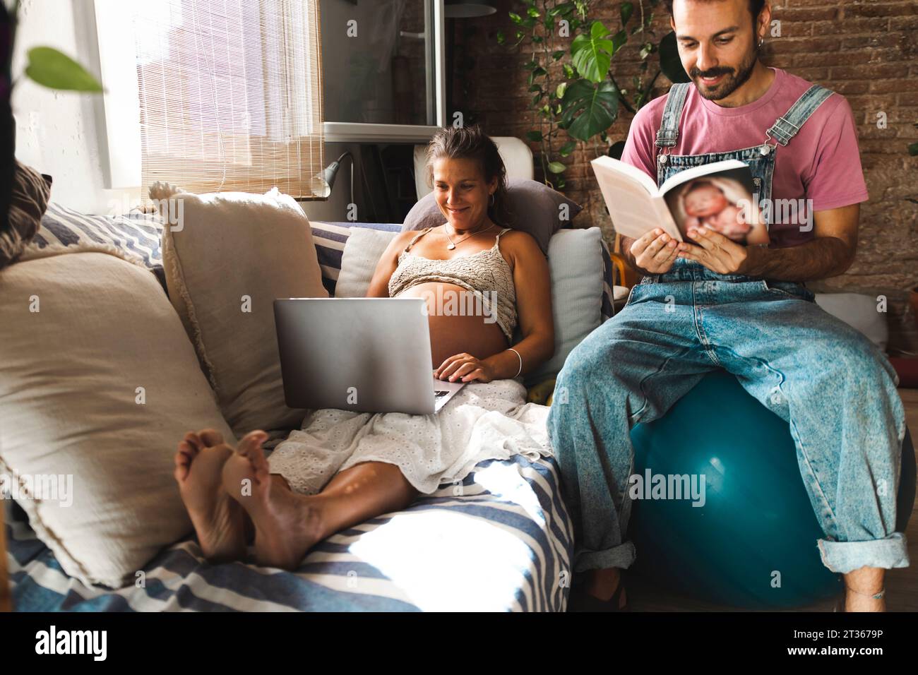 Lächelnde schwangere Frau mit Laptop und Mann, der auf Fitnessball sitzt Stockfoto