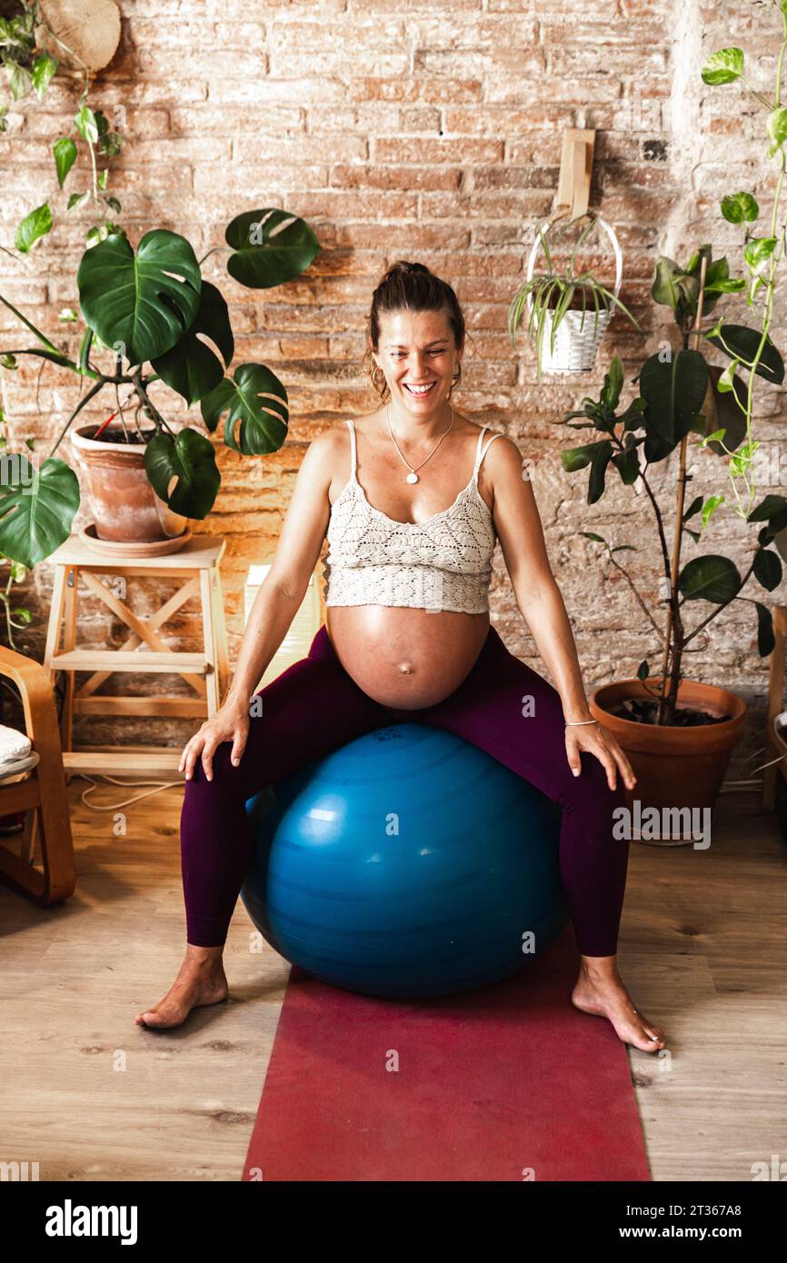 Lächelnde Frau, die zu Hause auf Fitnessball sitzt Stockfoto