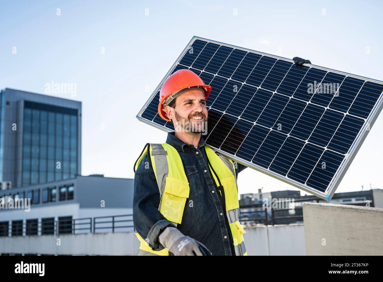 Ingenieur trägt Arbeitskleidung, der Solarpanel auf der Schulter auf der Terrasse trägt Stockfoto