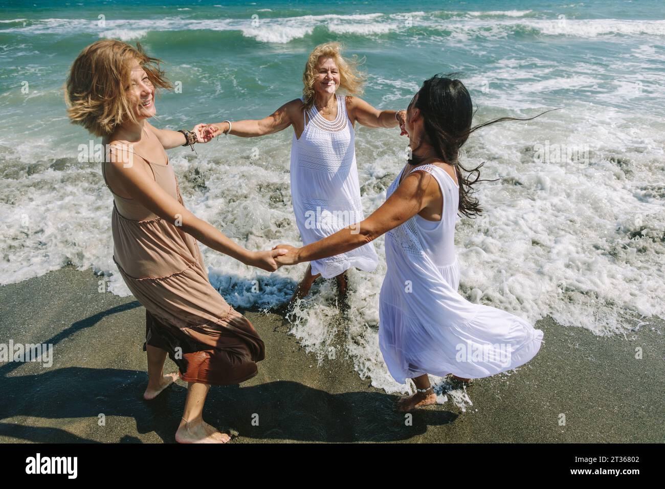 Fröhliche Freunde, die Hände halten und am Strand in rosiger Nähe des Meeres Ring spielen Stockfoto