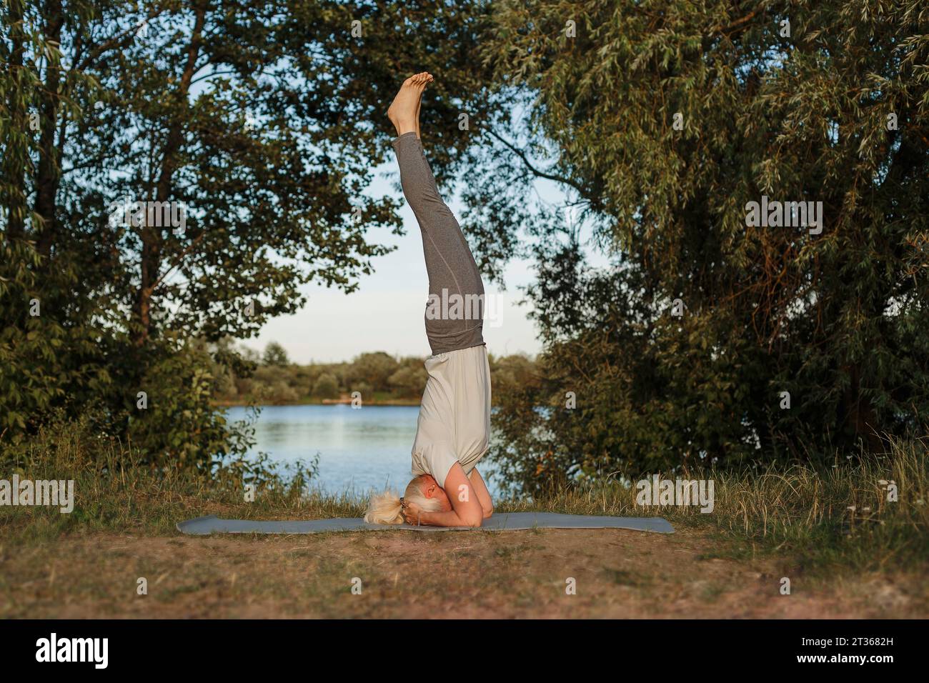Reife Frau übt Kopfstand-Yoga auf Matte am Seeufer Stockfoto