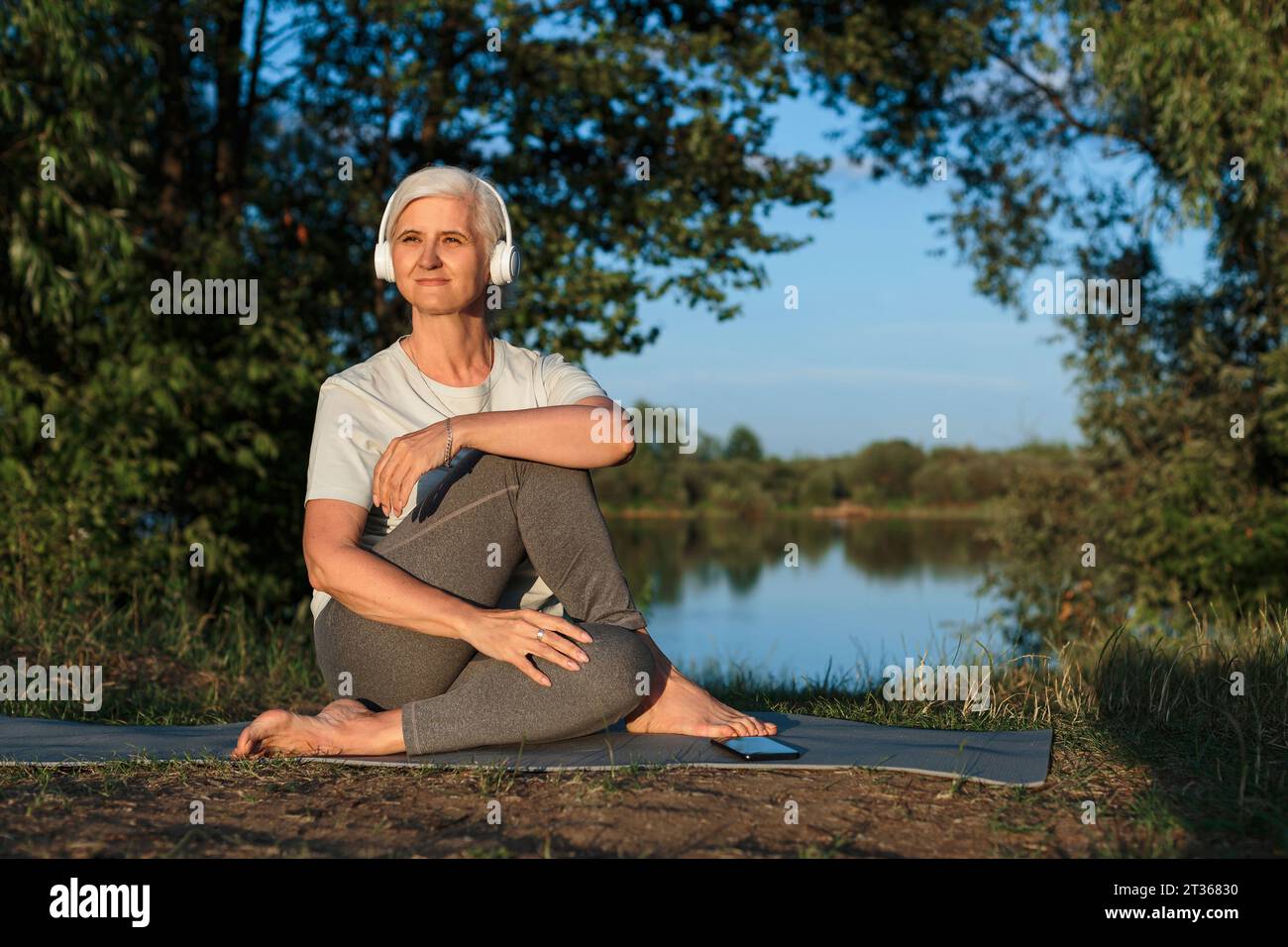 Reife Frau, die Musik hört und auf Yogamatte trainiert Stockfoto