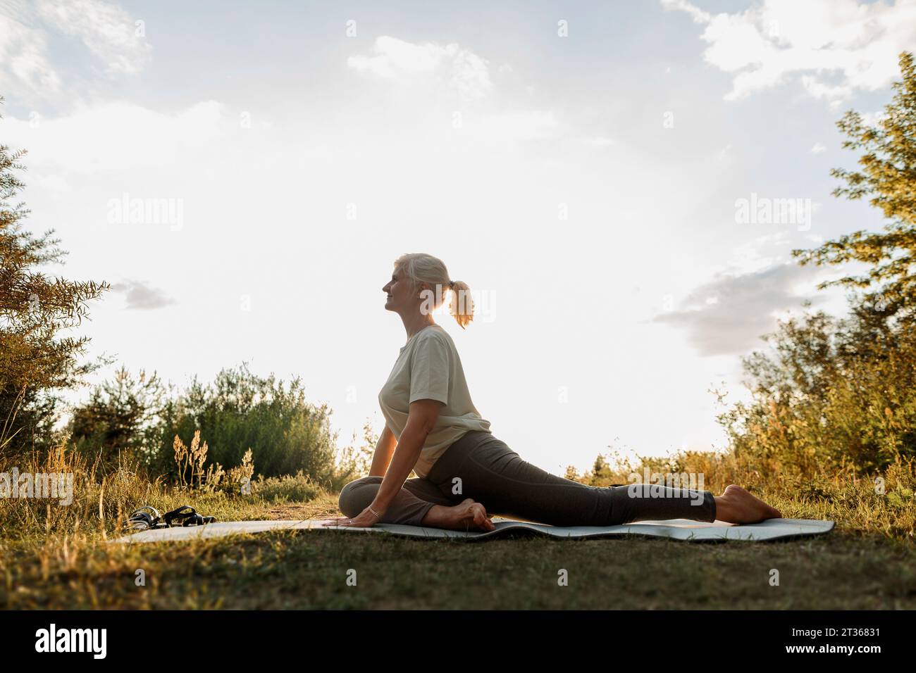 Frau übt Yoga auf Matte in der Nähe von Pflanzen Stockfoto