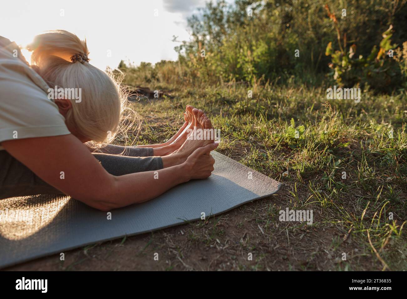 Reife Frau übt Yoga auf Matte bei Sonnenuntergang Stockfoto
